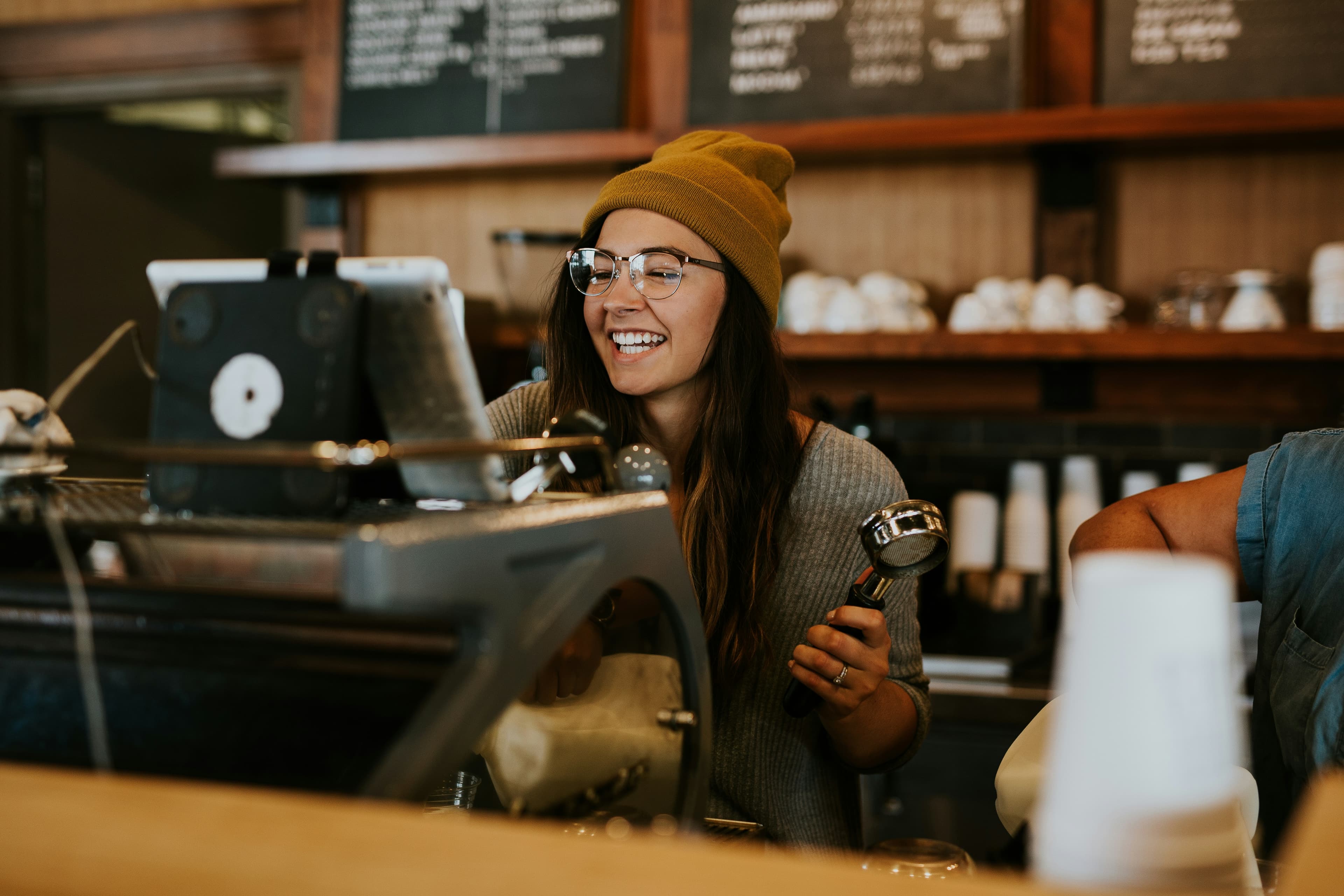 A barista smiling behind the counter of her coffee shop